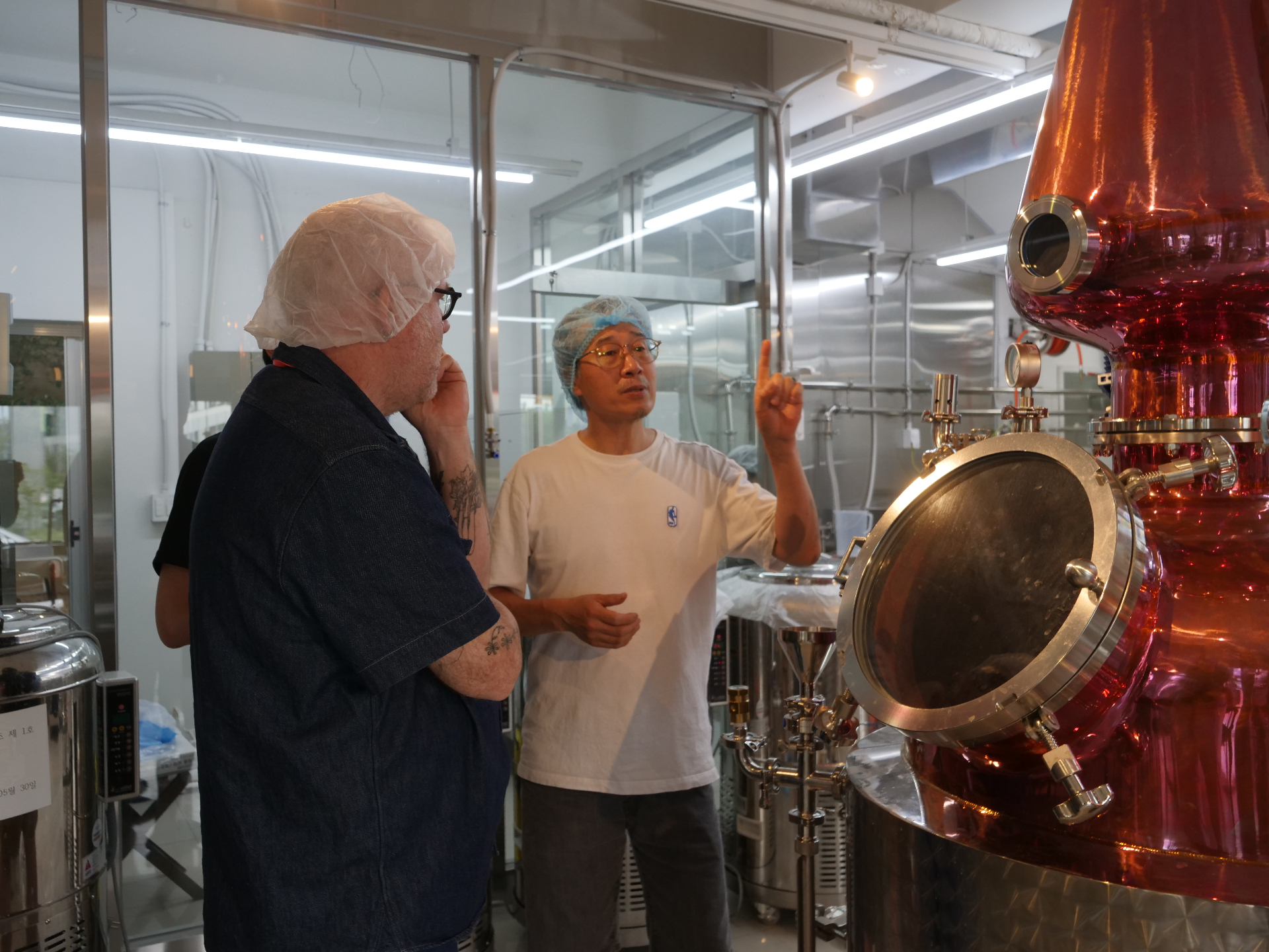 Technical discussion at modern Korean distillery with copper stills and glass observation windows