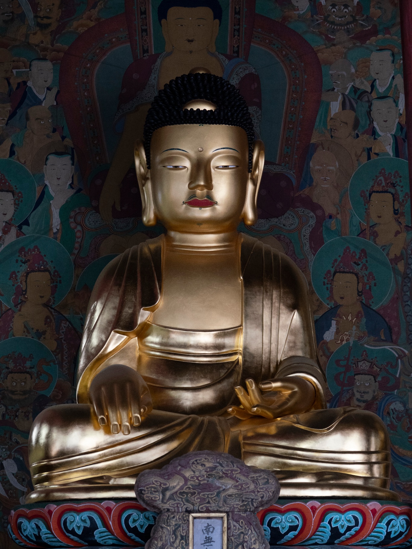 Golden Buddha statue in peaceful meditation surrounded by colorful temple artwork